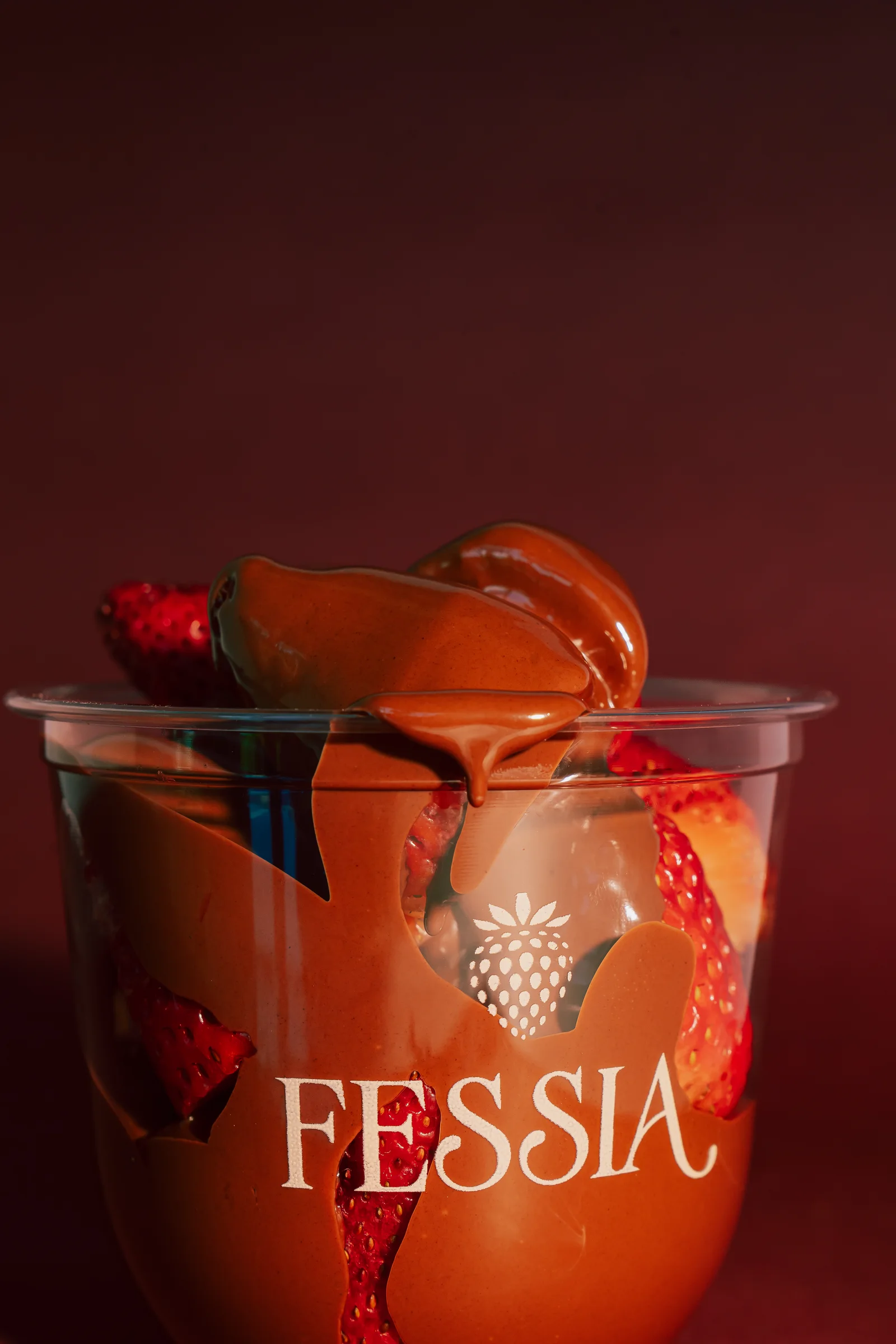 Fresas bañadas en chocolate en un vaso Fessia sobre fondo borgoña